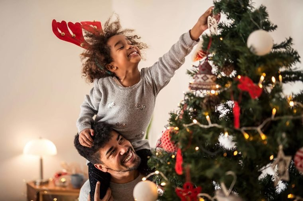 Father lifting up daughter on shoulders so she can put up the star on the Christmas tree