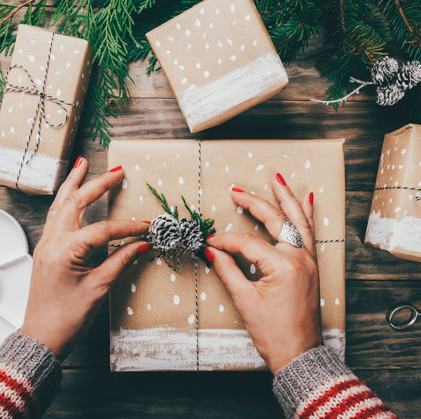 Person with red nail polish wrapping Christmas gifts with recycled paper and putting the presents under the Christmas tree.